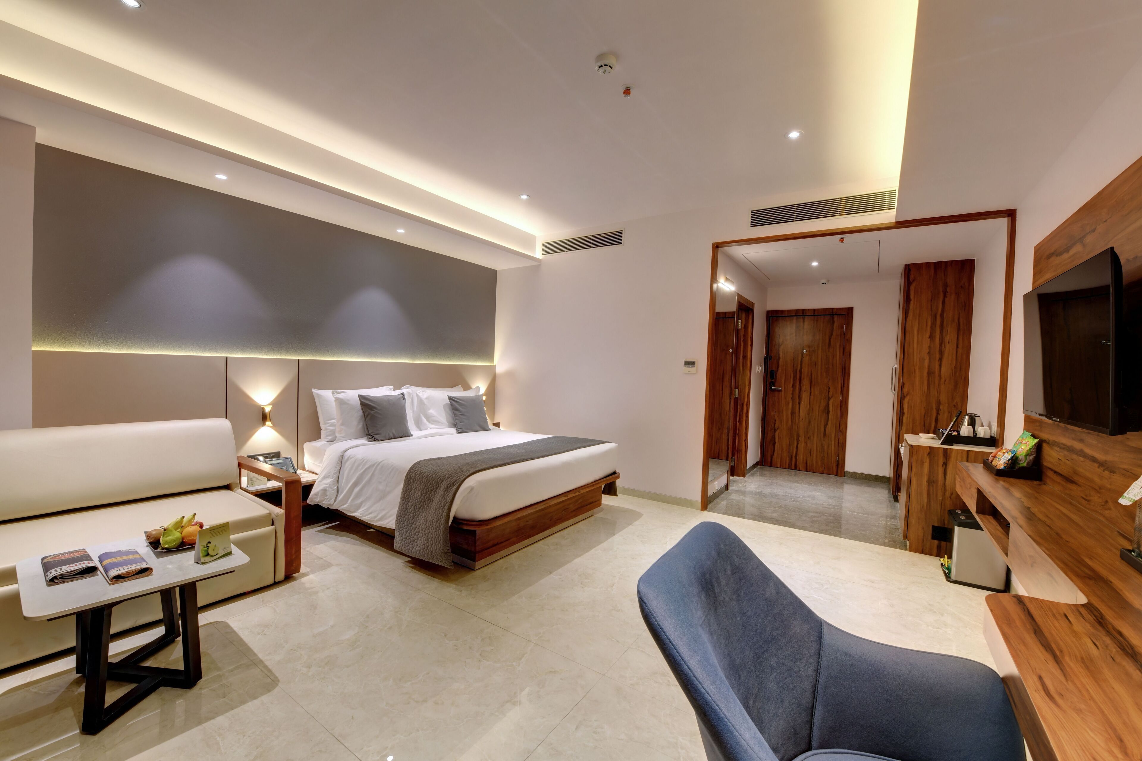A modern hotel room with a bed, a sofa, a desk, and a TV.