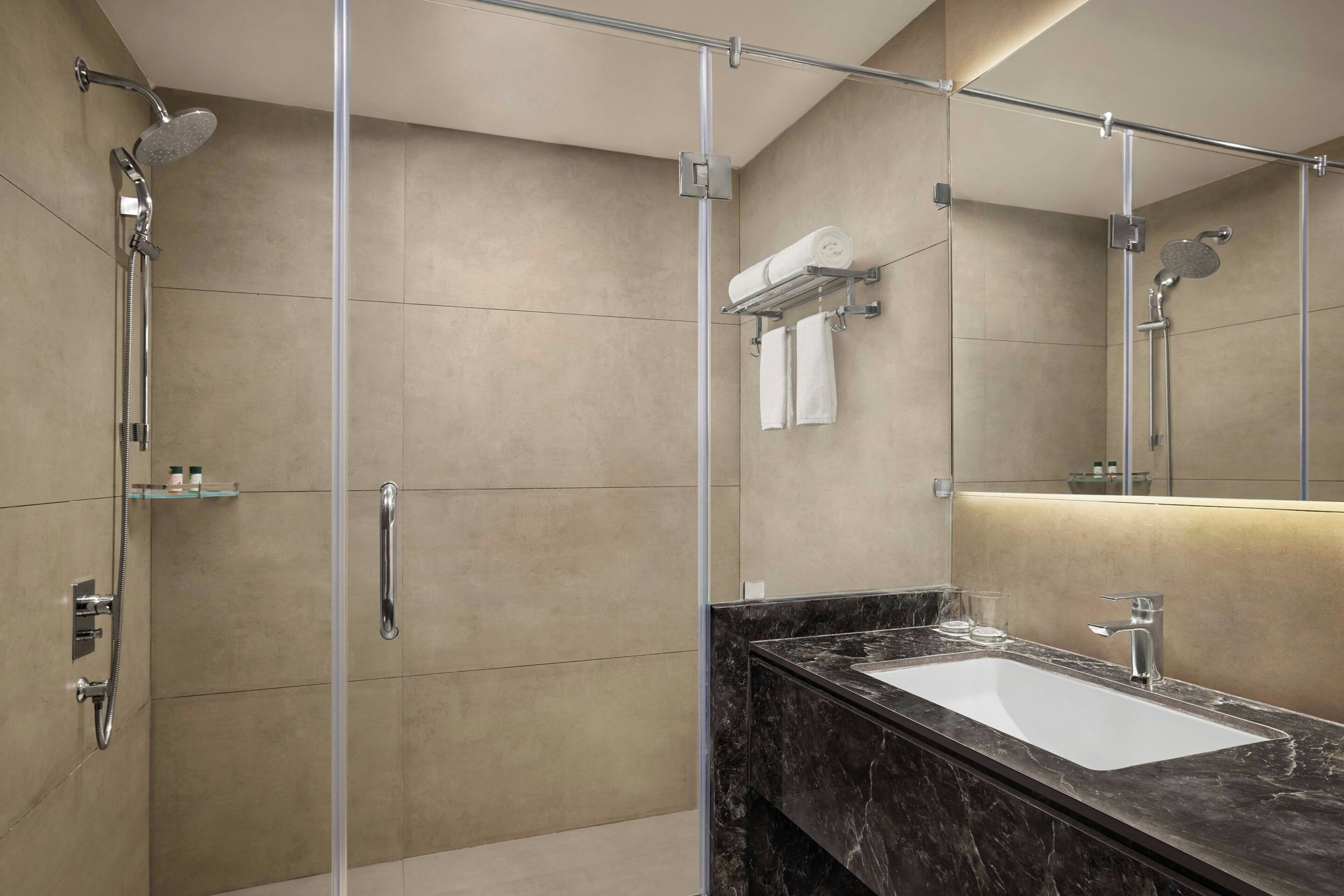 A modern bathroom with a glass-enclosed shower, a marble sink, and a large mirror.