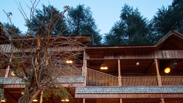A multi-story wooden building with balconies, stone walls, and a stone-paved entrance area. - Hotel  Negis Mayflower  (Manali)
