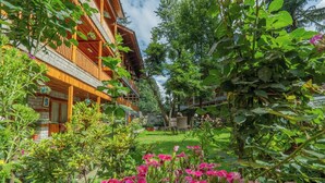 A wooden building with balconies, surrounded by lush greenery and flowering plants. - Hotel  Negis Mayflower  (Manali)