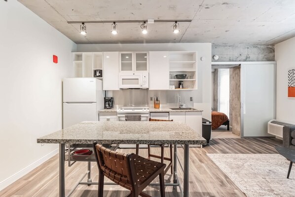 A modern kitchen with white cabinets, a granite countertop, and a dining area with a table and chairs.