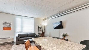 A modern living room with a large granite table, a gray sofa, a TV mounted on the wall, and a potted plant. - Explore Cleveland! Modern Apartment in the City (Cleveland)