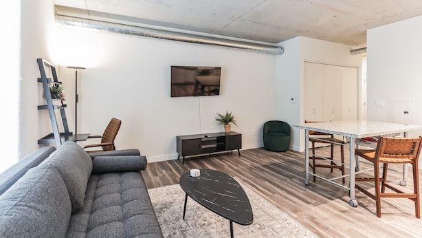 Una sala moderna con un sofá, una mesa de centro, un televisor, un comedor con una mesa y sillas, y un mueble.