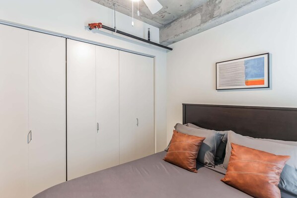 Un dormitorio con cama, almohadas, cabecera, armario y un cuadro enmarcado en la pared.