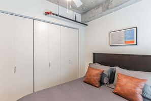 Een slaapkamer met een bed, kussens, een hoofdeinde, een kledingkast en een ingelijste foto aan de muur.