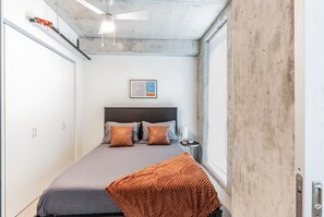 A bedroom with a bed, pillows, a bedside table, a ceiling fan, and a window.