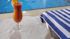 Área de piscina com espreguiçadeira e um copo de bebida tropical.