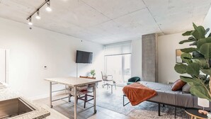 Una habitación moderna y bien iluminada con área de cocina, una mesa de comedor, una cama grande y un televisor montado en la pared.