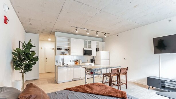 Un apartamento moderno con kitchenette, comedor, sala de estar con sofá y televisor montado en la pared.