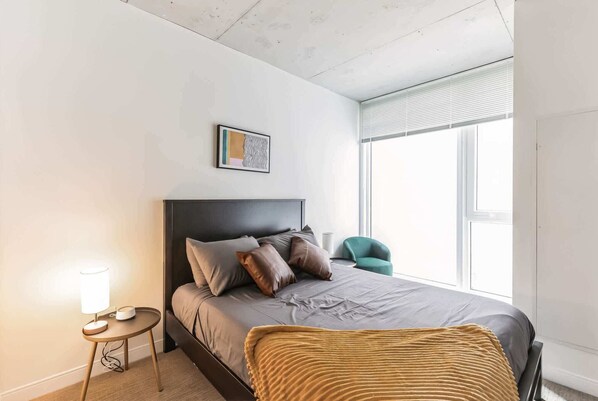 Ein modernes Schlafzimmer mit Bett, Nachttischlampe und einem Fenster mit Jalousien.