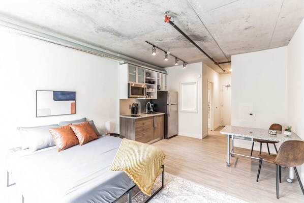 A modern apartment with a large bed, a kitchenette, a dining area, and a bathroom.