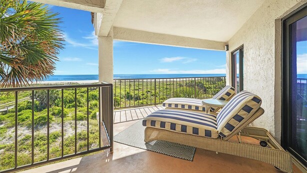 A balcony with a view of the ocean, a wicker sofa with striped cushions, and a small table. - 3 bedroom Ocean Front with amazing ocean views! (Saint Augustine)