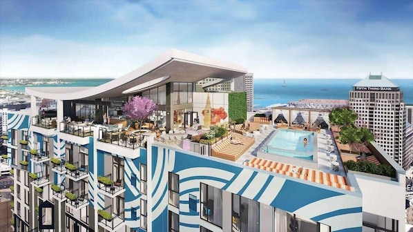 A modern hotel with a rooftop pool, a view of the sea, and a prominent bank building nearby.