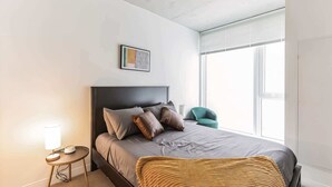 A modern bedroom with a bed, bedside lamp, and a window with blinds. - Central apartment with double queen beds (Cleveland)