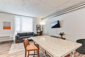 A modern living room with a large granite table, a gray sofa, a TV mounted on the wall, and a potted plant. - Unwind in Comfort—Stylish DT Cleveland Getaway (Cleveland)