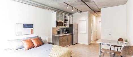 A modern apartment with a large bed, a kitchenette, a dining area, and a bathroom.