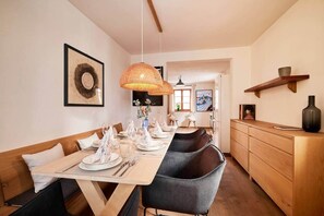 A dining area with a long table set for a meal, a hanging woven light fixture, and a wooden cabinet with a vase.