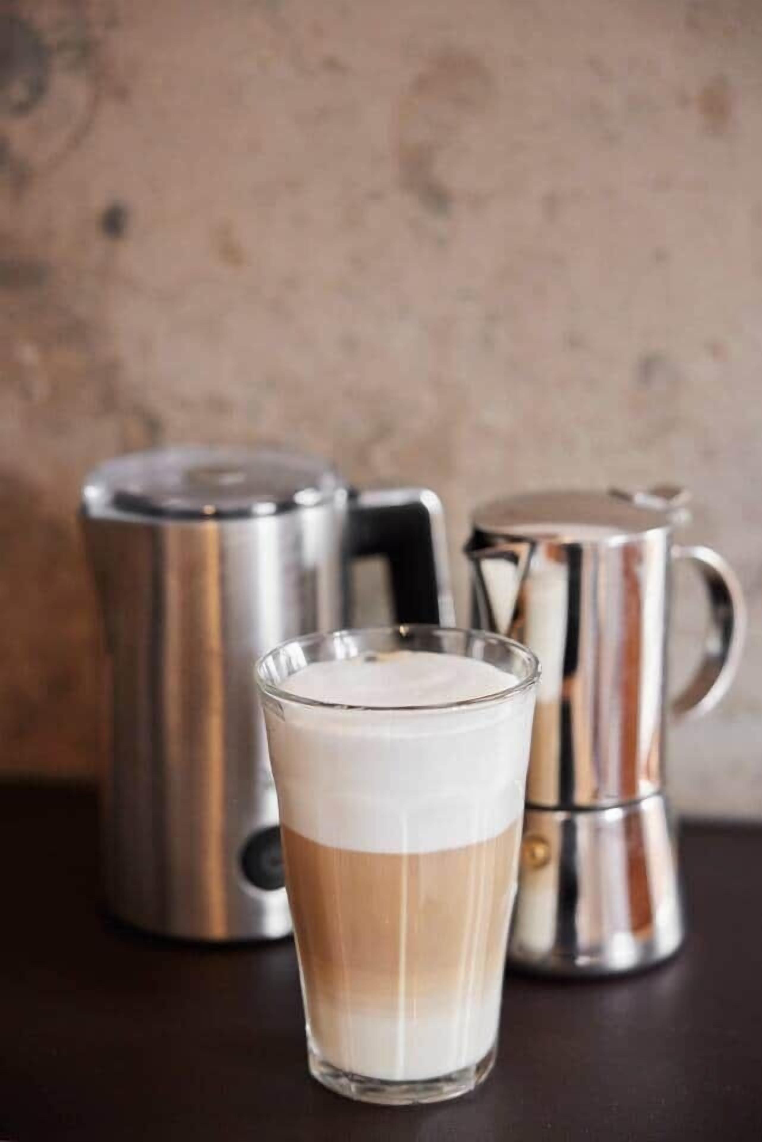 A glass of layered beverage with a metallic coffee maker in the background.