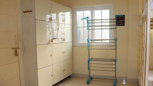 A room with a large cabinet, a window, and a metal drying rack. - Satshree Kothi (Varanasi)