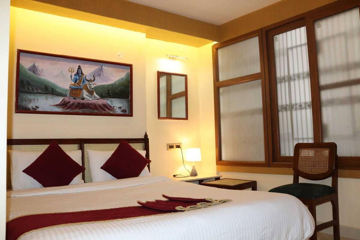 Habitació d'hotel amb un llit, una nit, una taula de nit, un quadre i una finestra amb persianes.