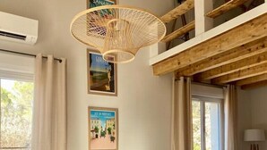 Un coin repas avec une table en bois, des chaises noires et en osier, et un luminaire tressé.