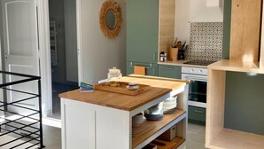 Une cuisine moderne avec des meubles blancs, un plan de travail en bois et une étagère intégrée. On y trouve deux suspensions lumineuses, un miroir rond et un pare-feu décoratif.