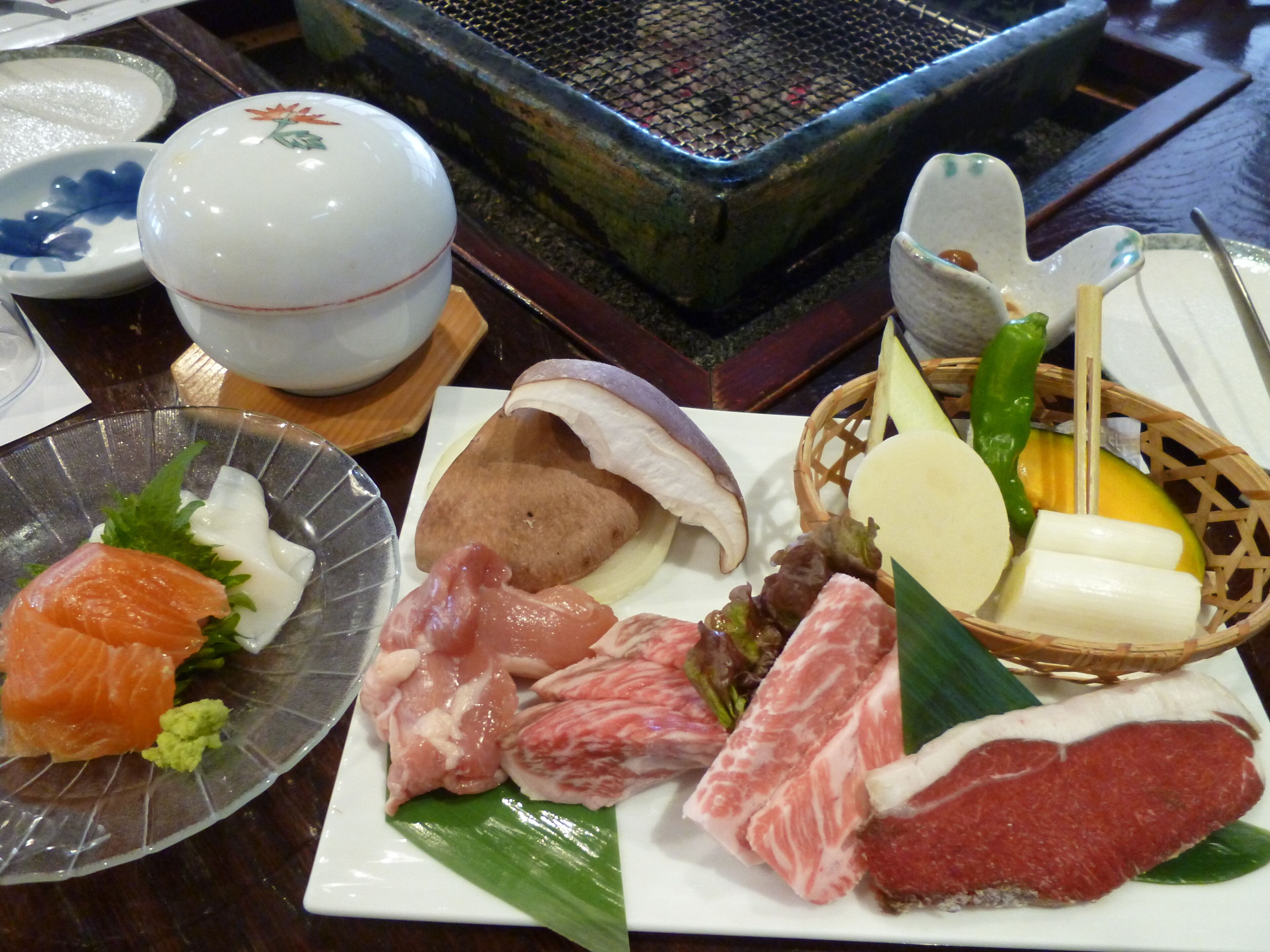 A variety of raw meats and fish on a plate, a bowl, and a basket with vegetables.
