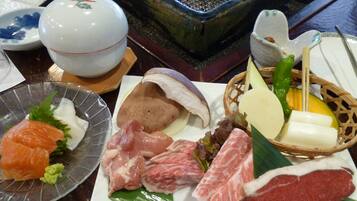 A variety of raw meats and fish on a plate, a bowl, and a basket with vegetables.