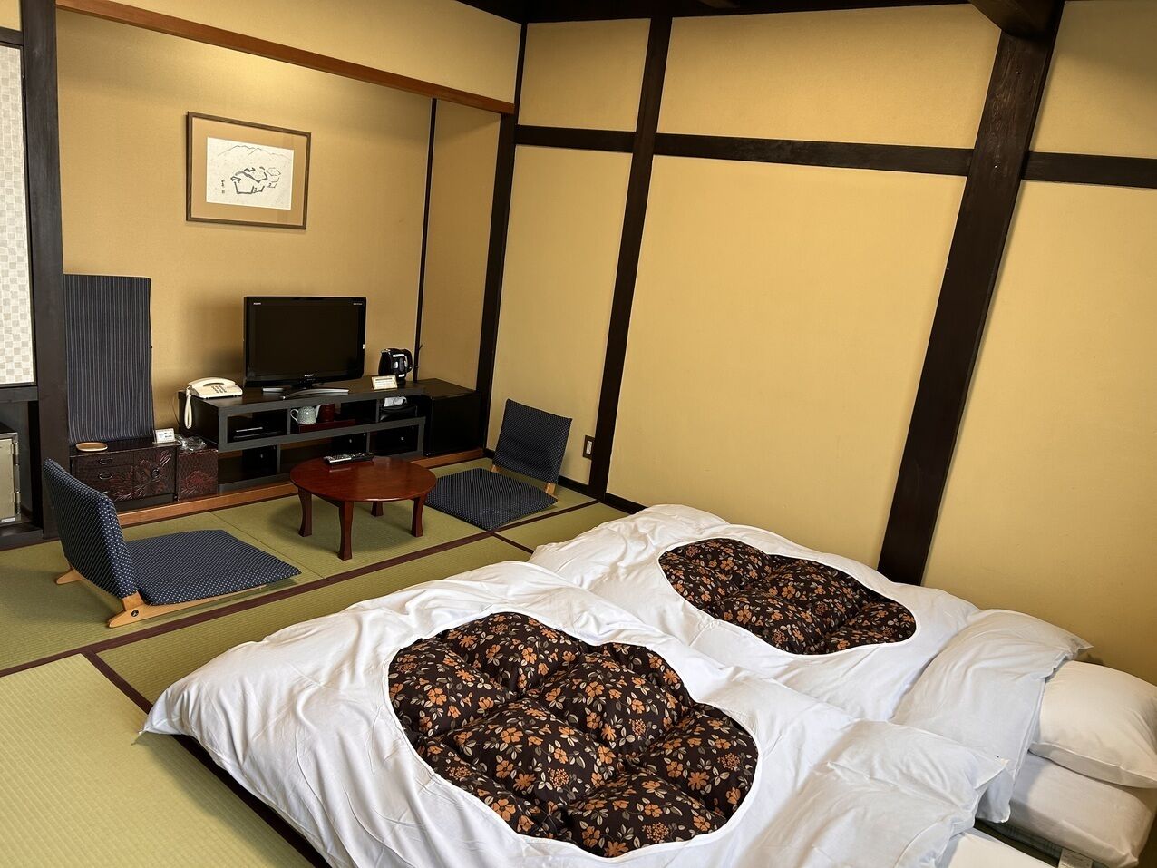 Una habitación tradicional japonesa con suelo de tatami, una mesa baja, un sofá y una cama con almohadones estampados con motivos florales.