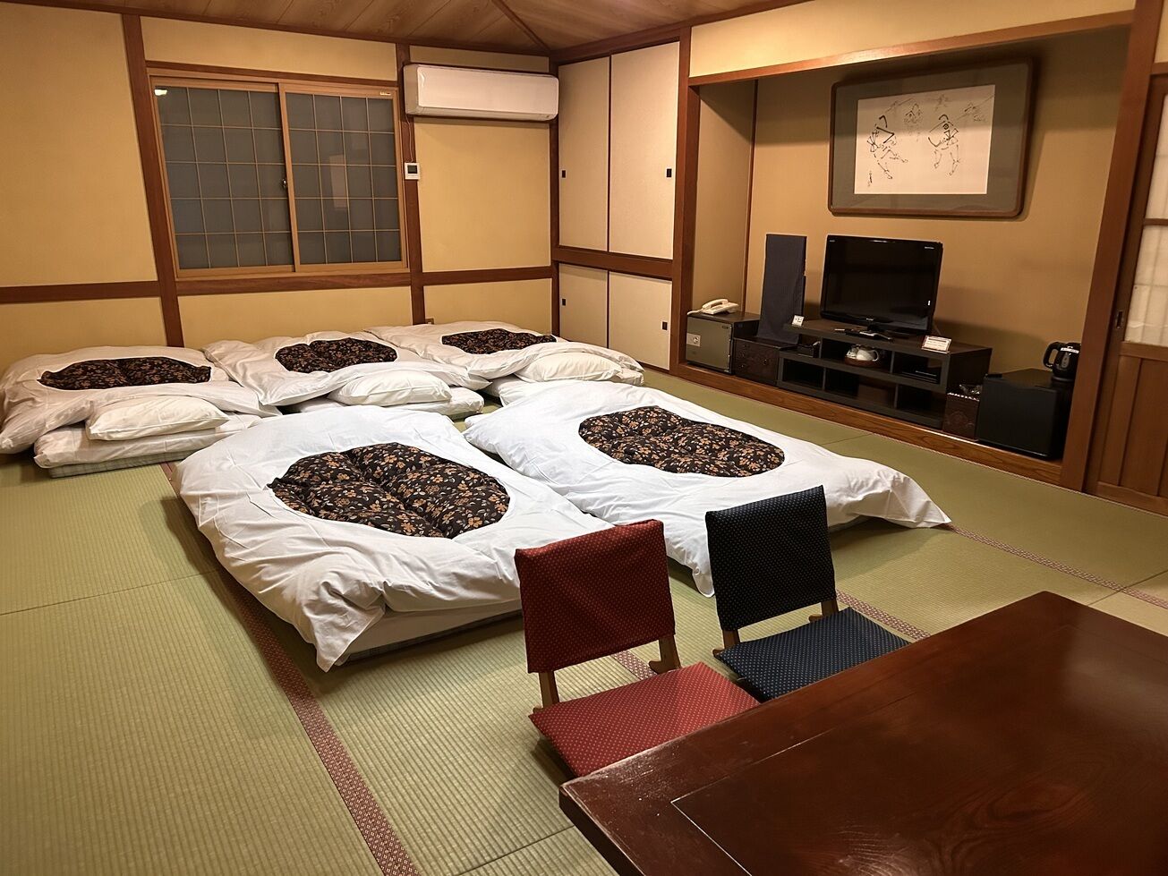 Una habitación japonesa tradicional con suelo de tatami, una mesa de madera baja y futones con almohadas.