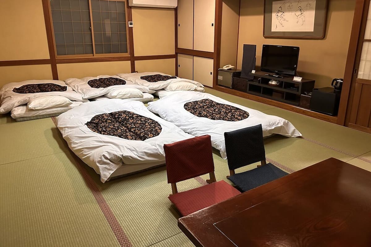 A traditional Japanese room with tatami flooring, a low wooden table, and futons with pillows.
