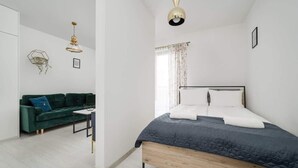 A modern bedroom with a bed, a green sofa, a small table, and a hanging light fixture. - Modern Studio in the Center | Balcony | Close to Market Square (Wroclaw)
