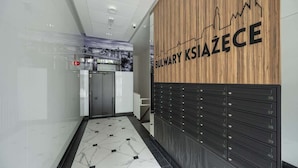 A modern hallway with a wooden wall displaying the name 'BULWARY KSIAZEC' and a black locker area with numbered compartments. - Modern Studio in the Center | Balcony | Close to Market Square (Wroclaw)