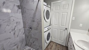 A bathroom with a shower, a washing machine, and a toilet. - ENTIRE UNIT | 2BR | Washer/Dryer | Sleeps 6 | Near Airport (Austin)