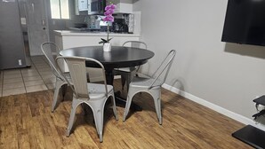 A dining area with a round table and four chairs, a kitchen in the background, and a TV mounted on the wall. - ENTIRE UNIT | 2BR | Washer/Dryer | Sleeps 6 | Near Airport (Austin)