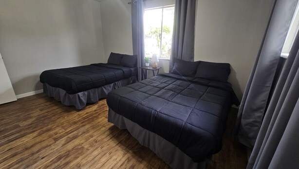 A bedroom with two beds, wooden flooring, and a window with curtains. - ENTIRE UNIT | 2BR | Washer/Dryer | Sleeps 6 | Near Airport (Austin)