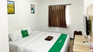 A hotel room with a bed, a desk, a television, and an air conditioning unit. - Bima Guest House (Malang)