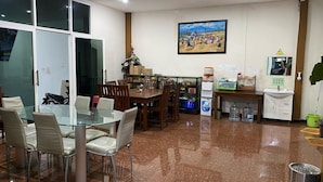 A dining area with a glass table and chairs, a kitchen area with a sink and cabinets, and a painting on the wall. - Bima Guest House (Malang)