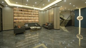 A modern lobby with a marble floor, a central seating area with sofas, a staircase, and a display wall with various items. - Kelley Hotel (Wuzhou)
