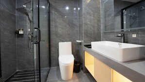 A modern bathroom with a glass-enclosed shower, a white toilet, and a large sink with a mirror above it. - Kelley Hotel (Wuzhou)