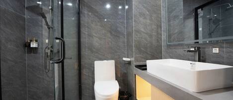 A modern bathroom with a glass-enclosed shower, a white toilet, and a large sink with a mirror above it.