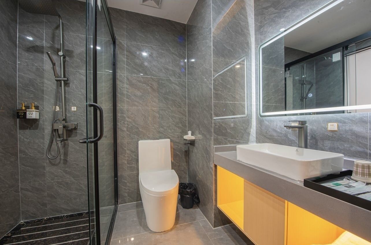 Un baño moderno con cabina de ducha de vidrio, inodoro blanco y tocador con un espejo grande.