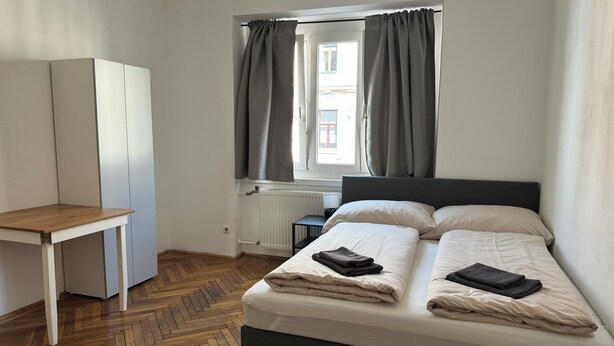 A bedroom with a bed, a desk, a wardrobe, and a window with curtains.