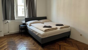 A bedroom with a bed, a radiator, a window with curtains, and a herringbone wooden floor.