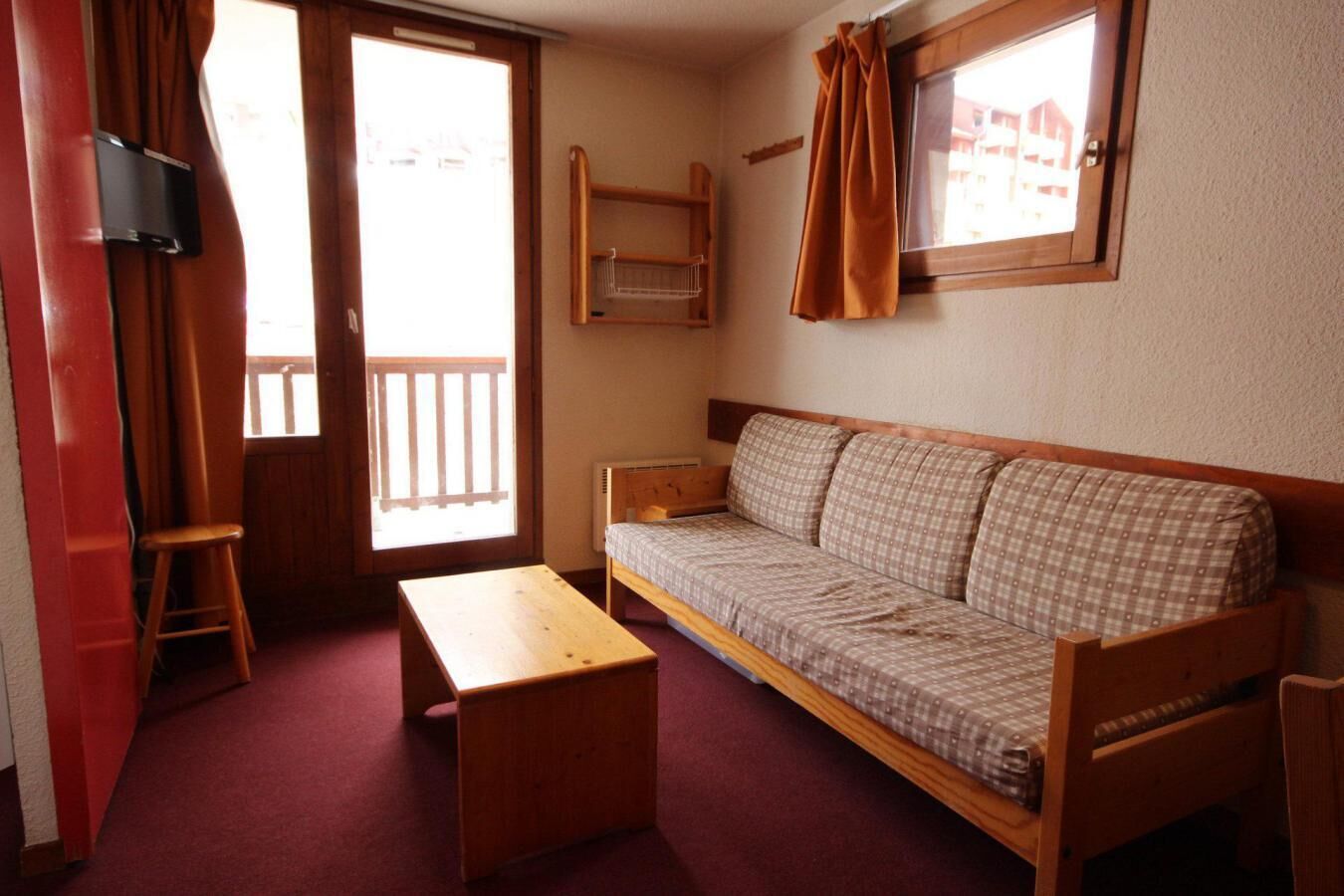 A small, cozy room with a wooden sofa, a wooden table, and a television mounted on the wall.