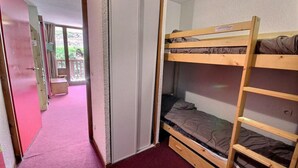 A bunk bed room with a red carpet, a wooden door, and a view of an outdoor balcony.