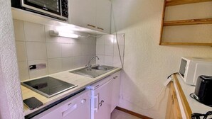 A compact kitchen with a microwave, stove, sink, and a small refrigerator.