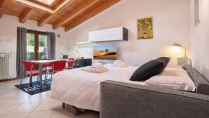 A hotel room with a bed, a desk with a chair, a TV, and a painting on the wall. - Apartment Ponte Tesina (Costermano)