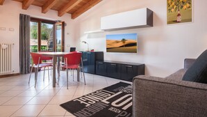 A modern living room with a dining area, featuring a wooden ceiling, a large window, a sofa, a dining table with red chairs, and a kitchen area with cabinets and a countertop. - Apartment Ponte Tesina (Costermano)