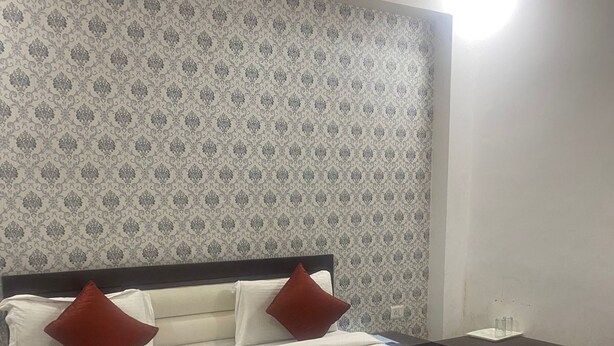 A neatly made bed with white and red bedding, a dark headboard, and a patterned wallpaper. - Hotel Avalon Palace  (New Delhi)